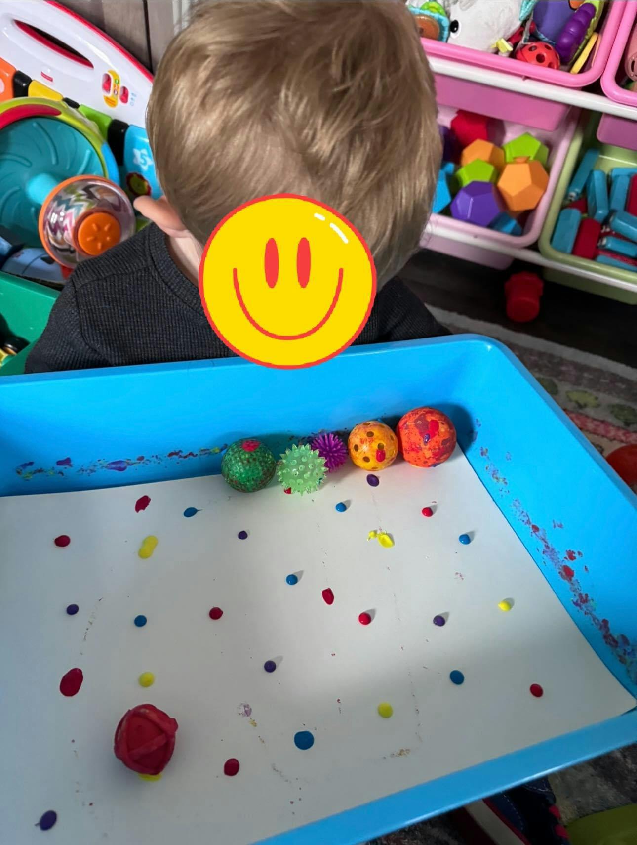 Child playing with colorful balls in a blue tray