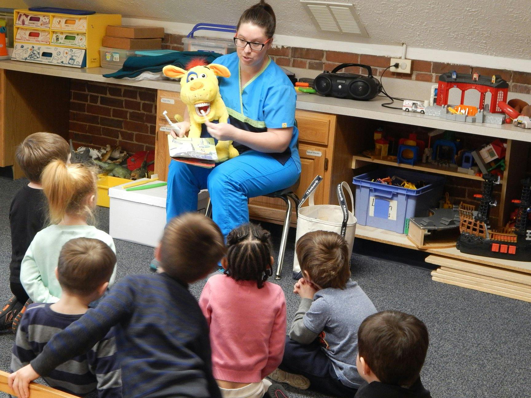 Person in scrubs holding a puppet for a group of children