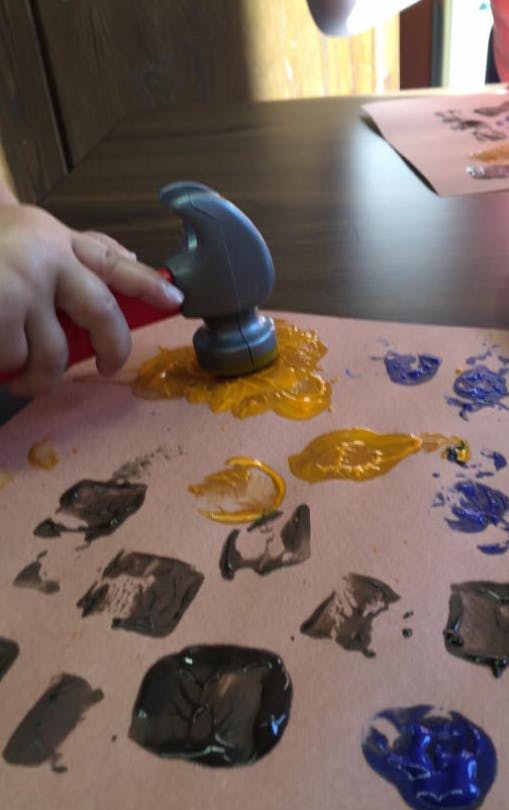 Child's hand holding a toy hammer, pressing it into yellow paint