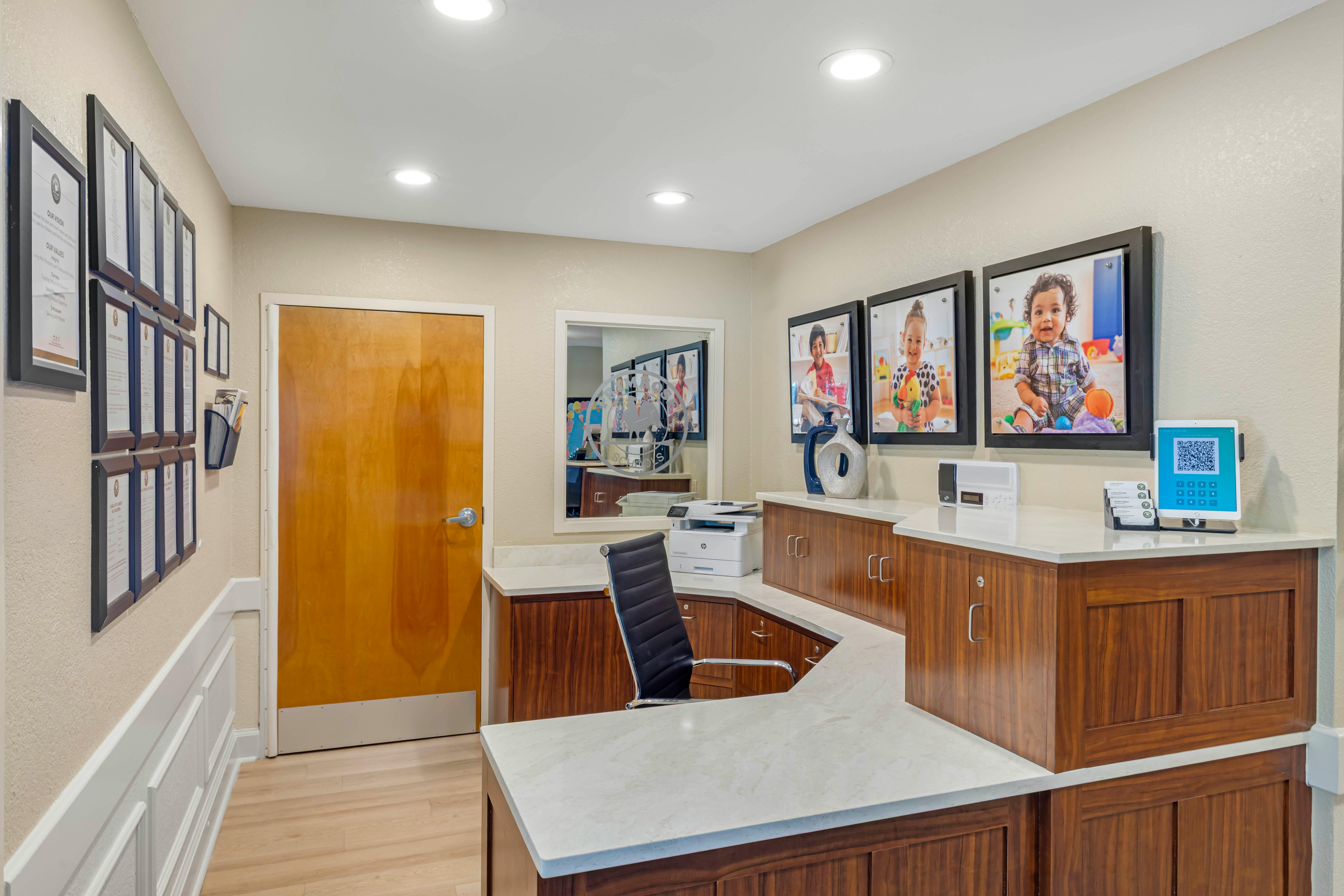 Reception desk with office chair, printer, and framed children's photos on the wall