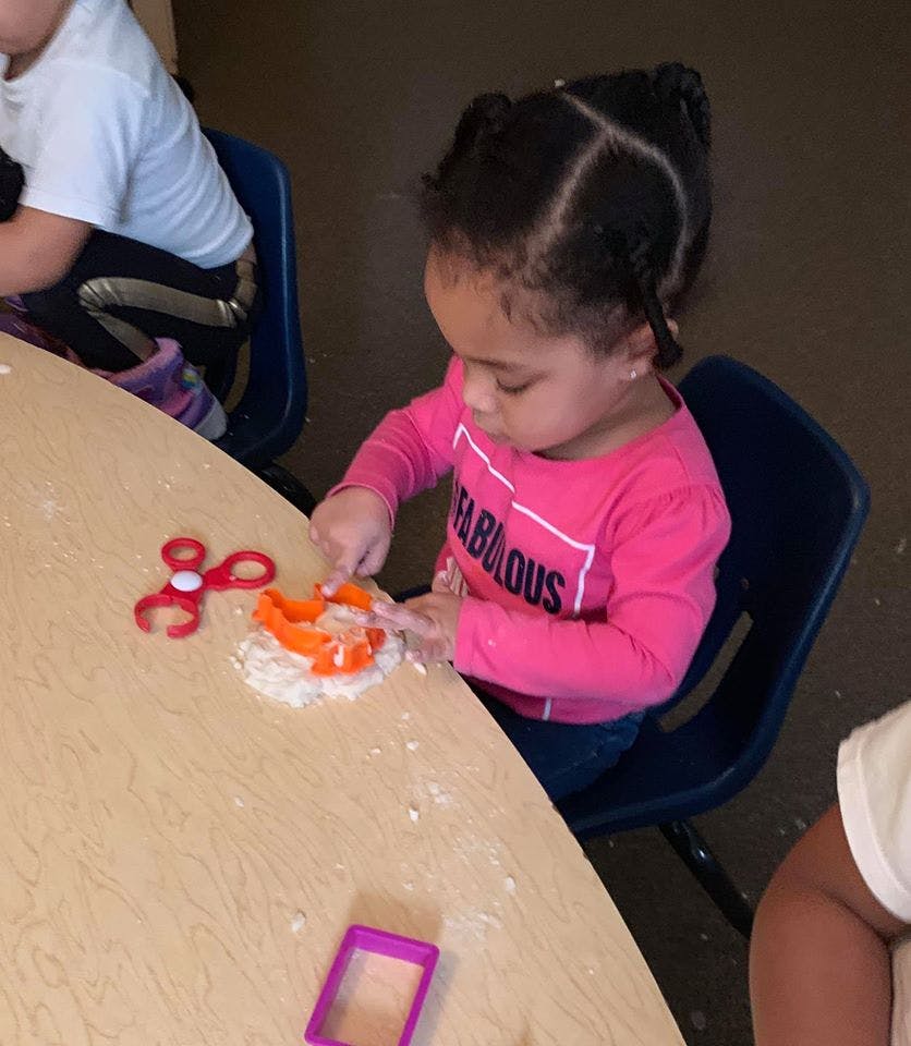 Child playing with cookie cutters and white powder on a table