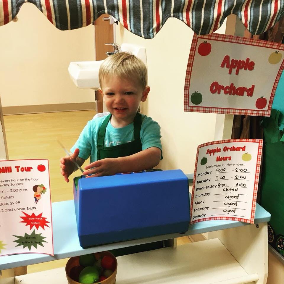 Child in an apron behind a counter with an "Apple Orchard" sign