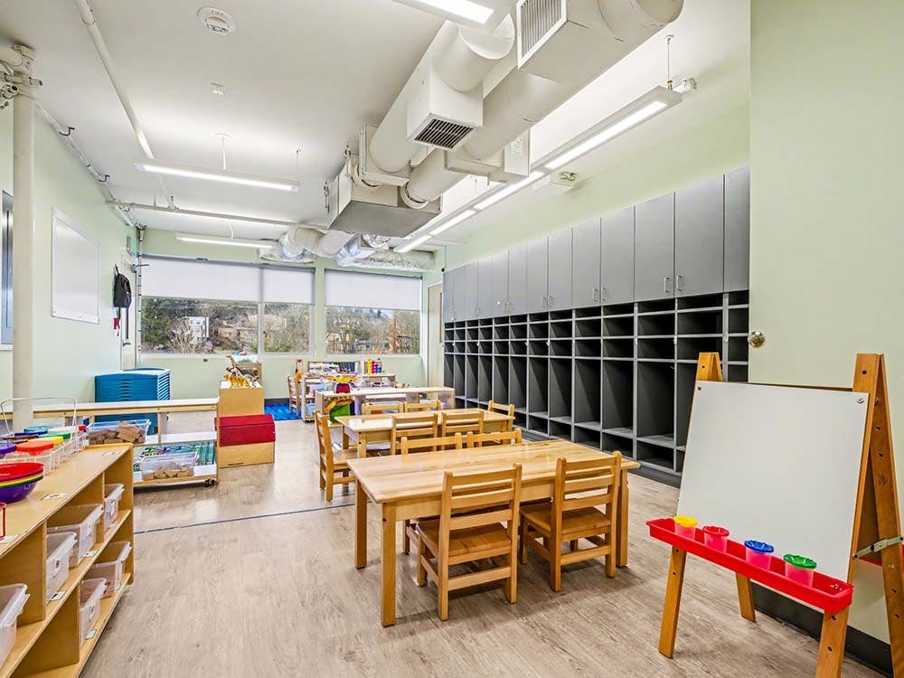 Empty classroom with small wooden tables and chairs, shelves, and cubbies