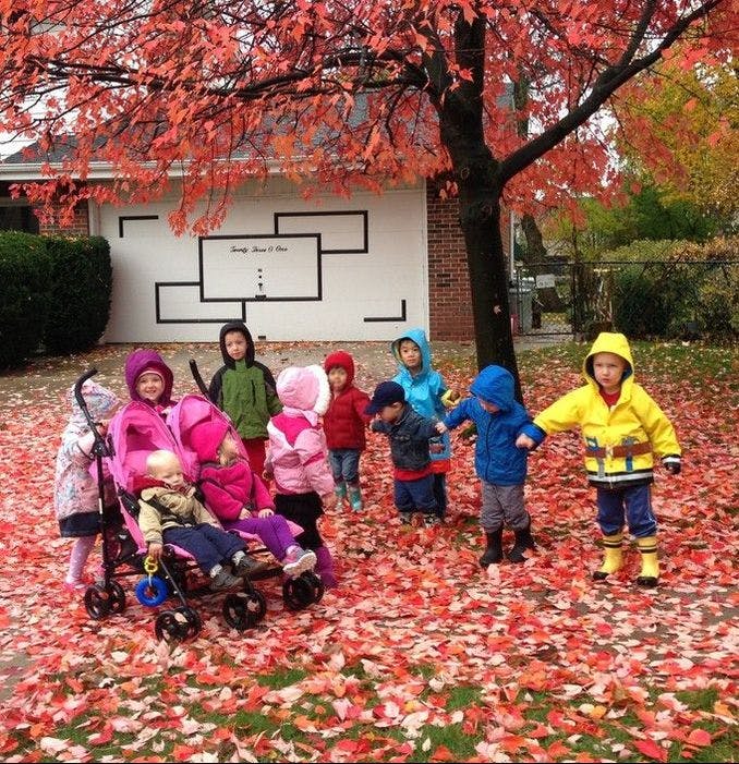 Children and strollers on a lawn covered in red autumn leaves