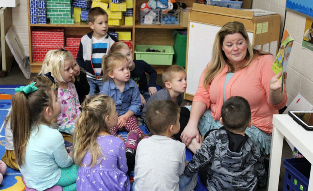 Adult reading a book to a group of children in a classroom