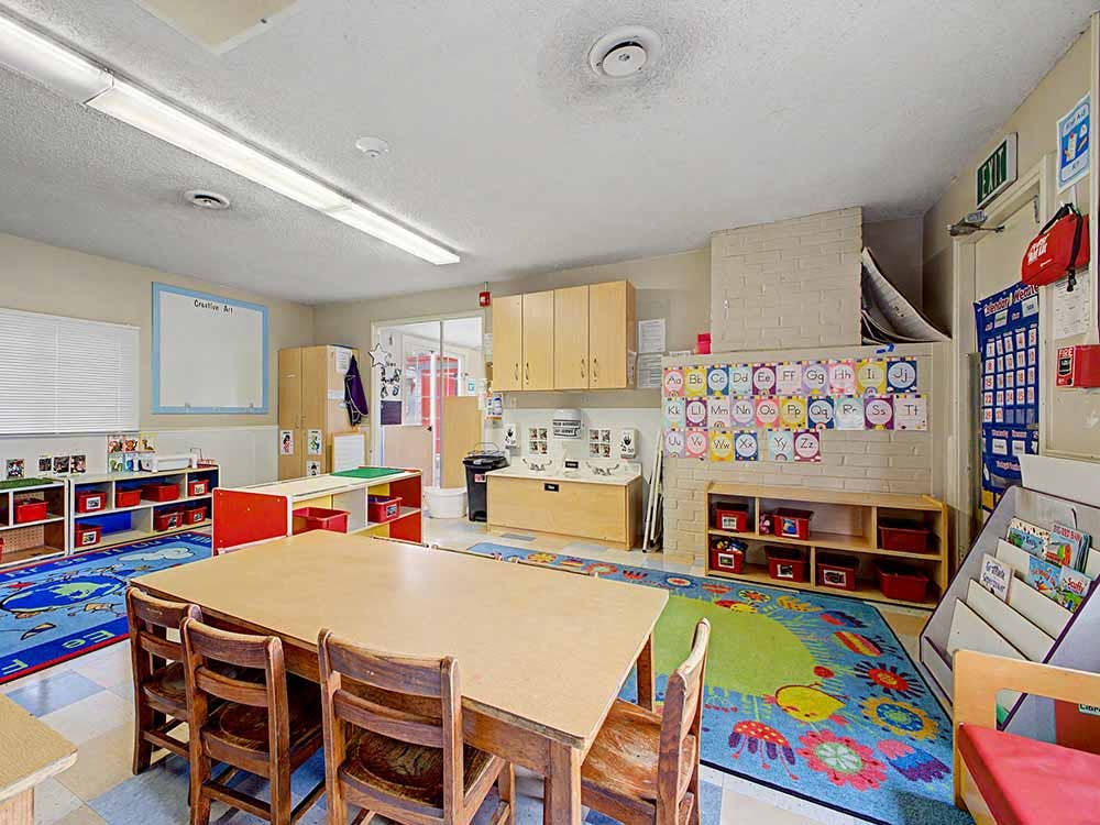 Empty classroom with small tables and chairs, alphabet chart on a brick wall