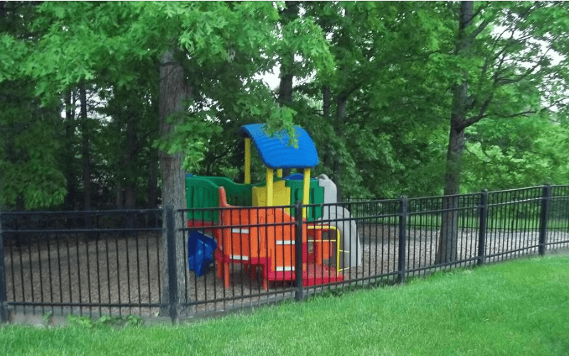 Colorful playground surrounded by a black fence and green trees