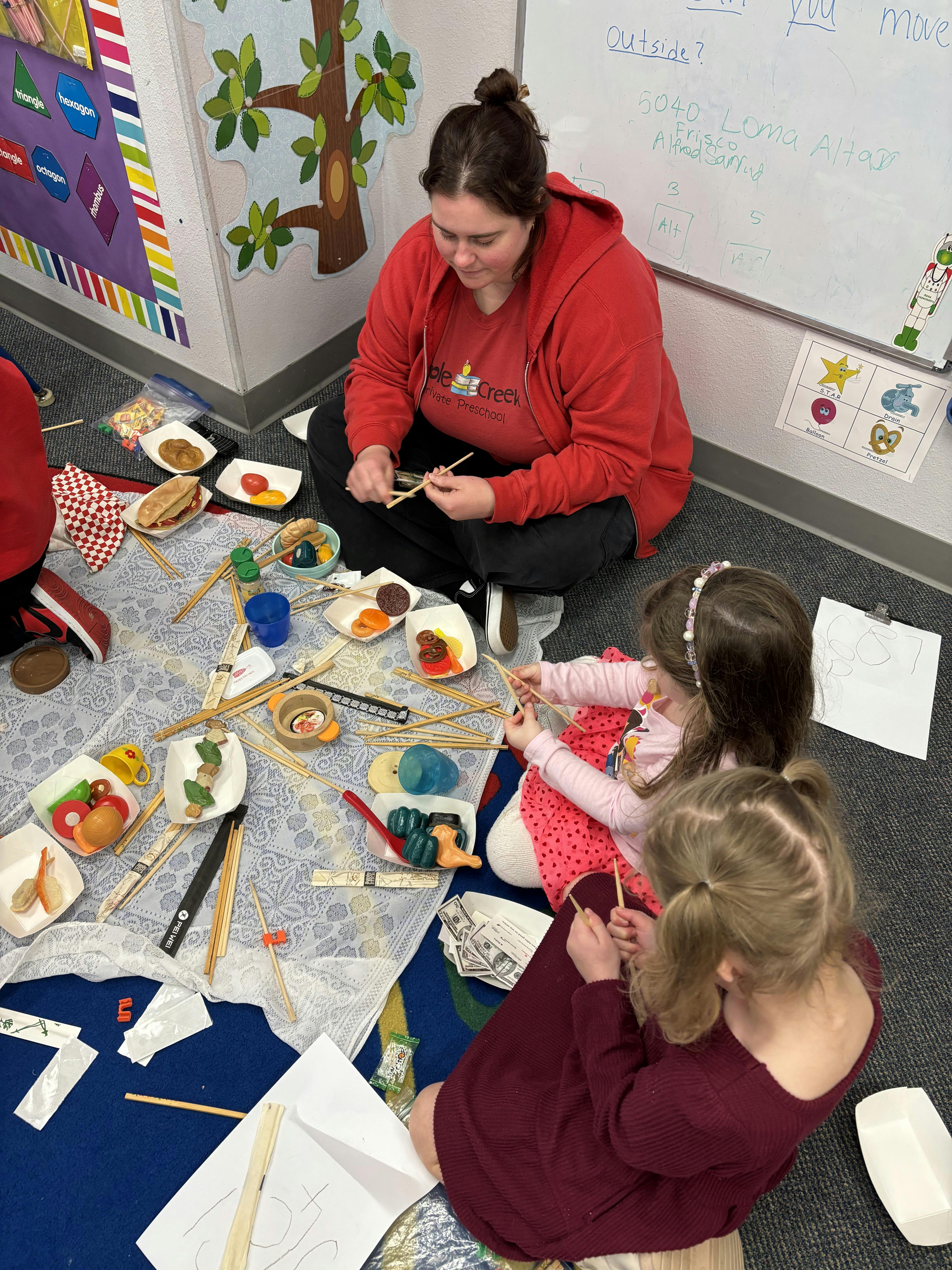 Person and two children sitting on floor making crafts with craft sticks
