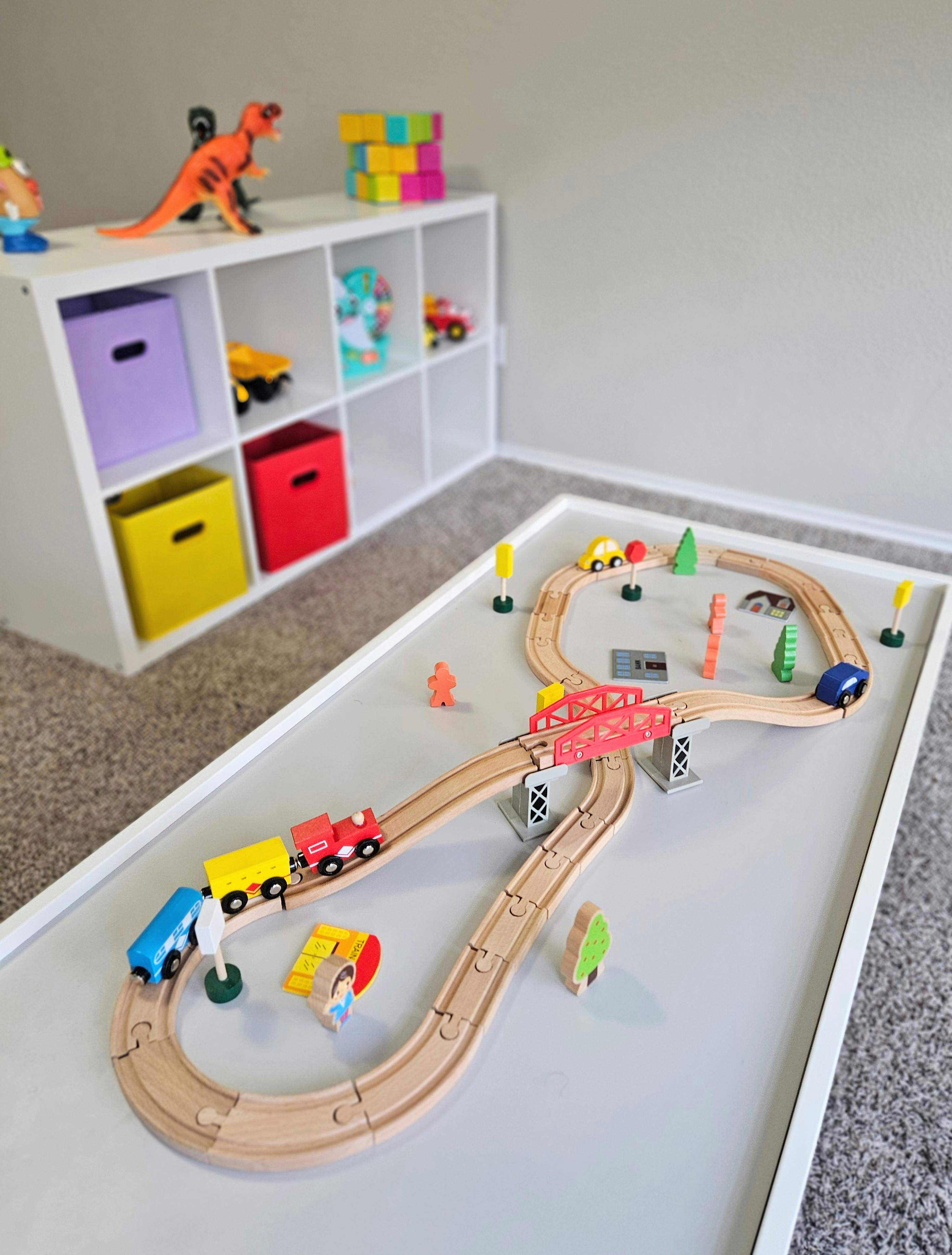 Wooden toy train set with tracks, bridge, and small figures on a play table