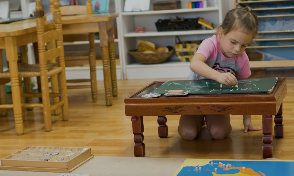 Child kneeling and drawing on a small table in a classroom