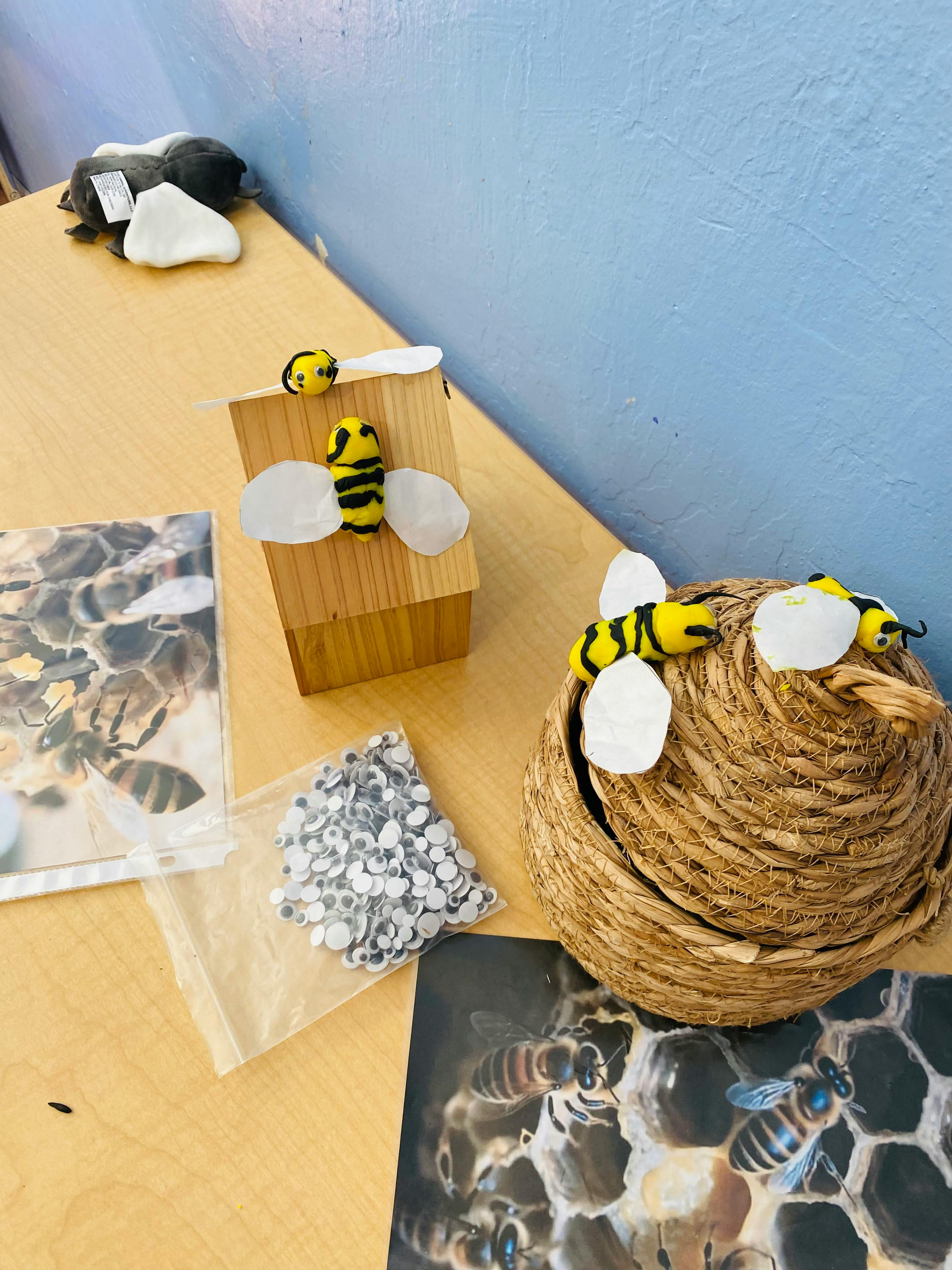 Craft bees on a wooden hive and basket with googly eyes and bee photos