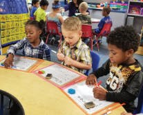 Three children drawing at a table in a classroom