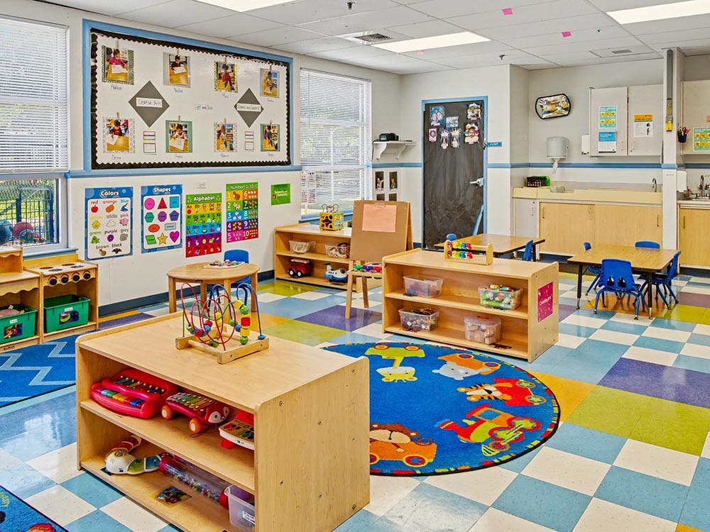 Classroom with small tables, shelves of toys, and colorful educational posters