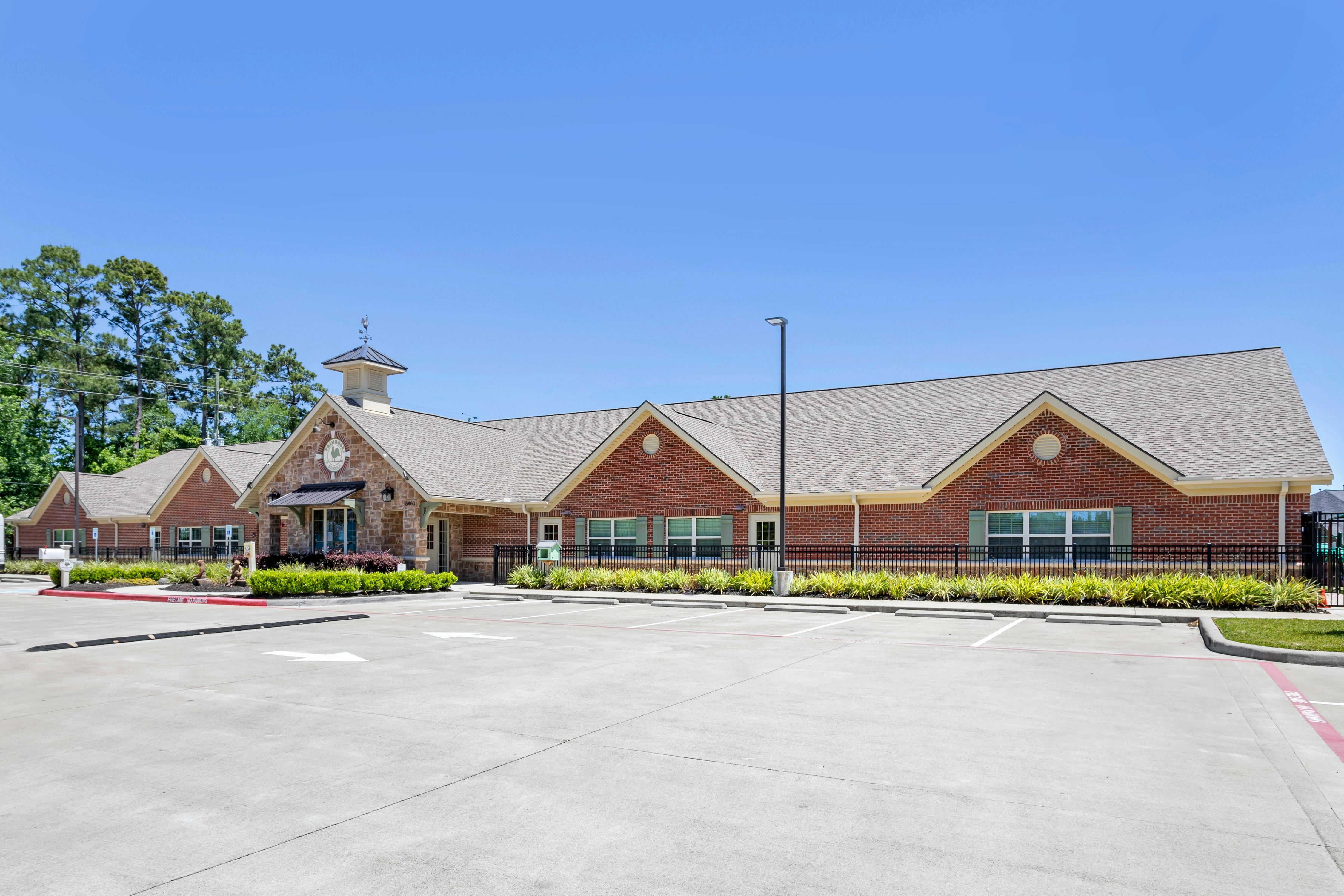 Brick building with gabled roofs and a cupola, a parking lot in the foreground