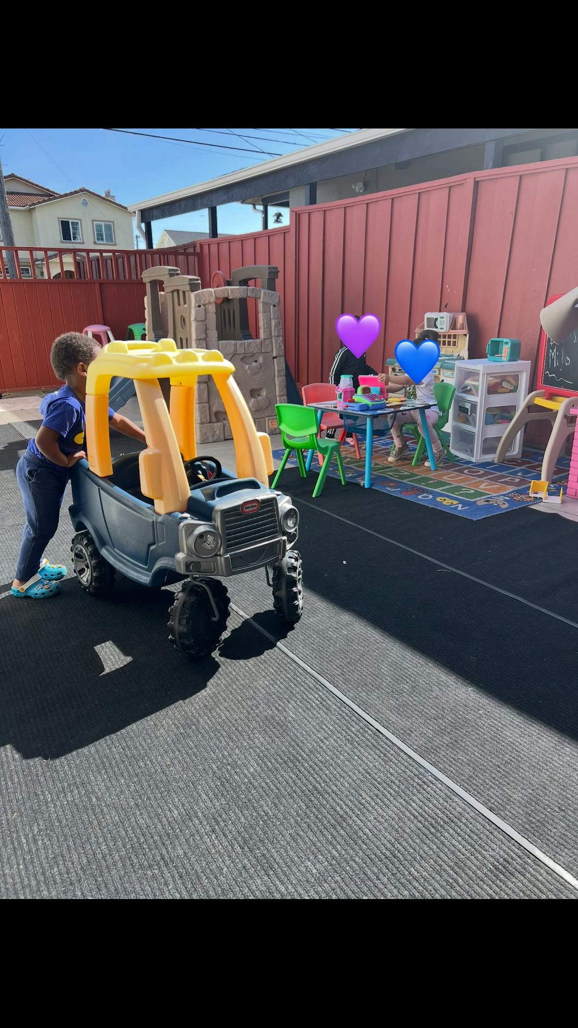 Child pushing a toy car in a fenced play area