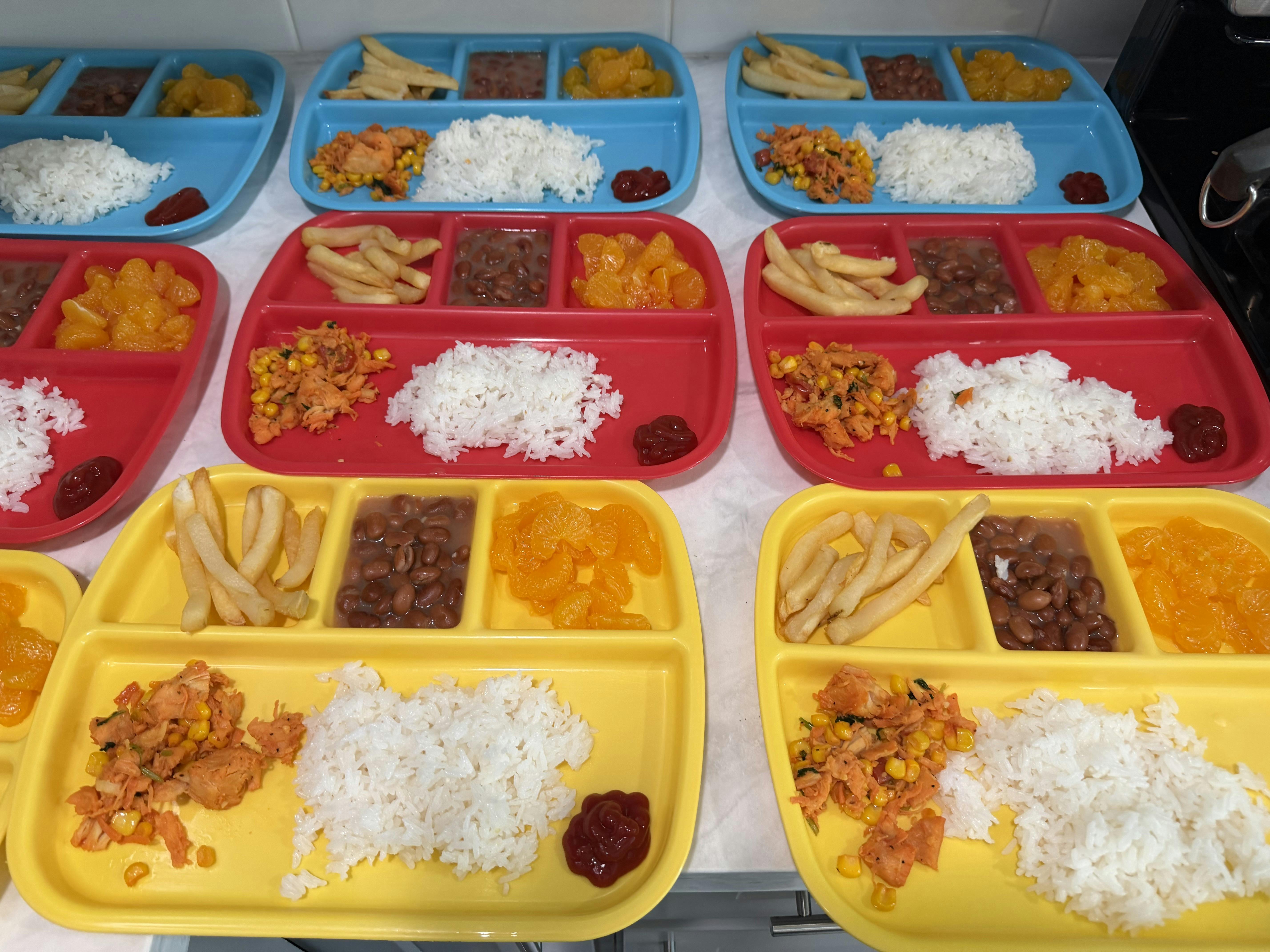 Multiple partitioned trays containing portions of rice, beans, fruit, and fries