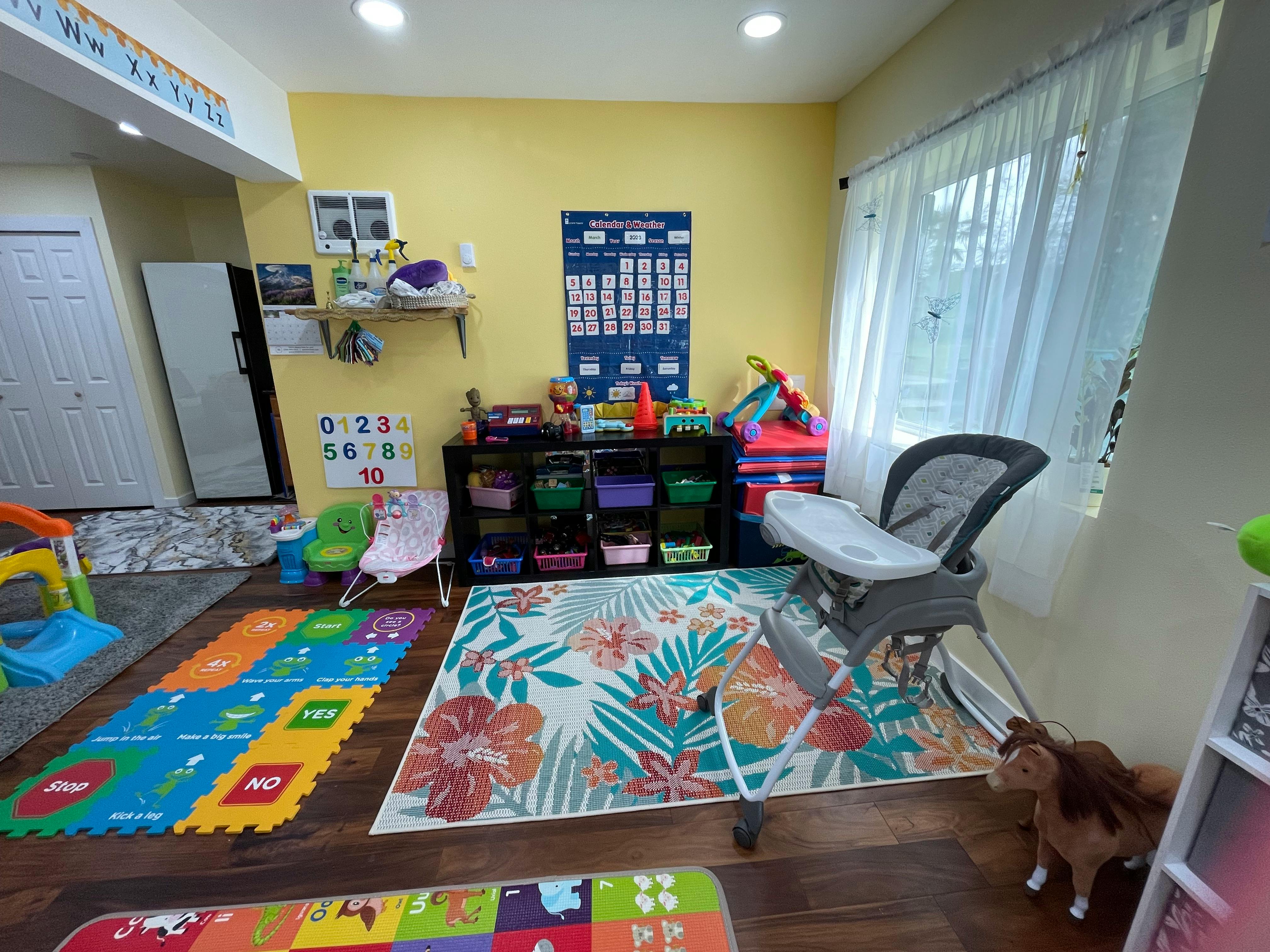 A room with colorful rugs, a high chair, and storage shelves with toys