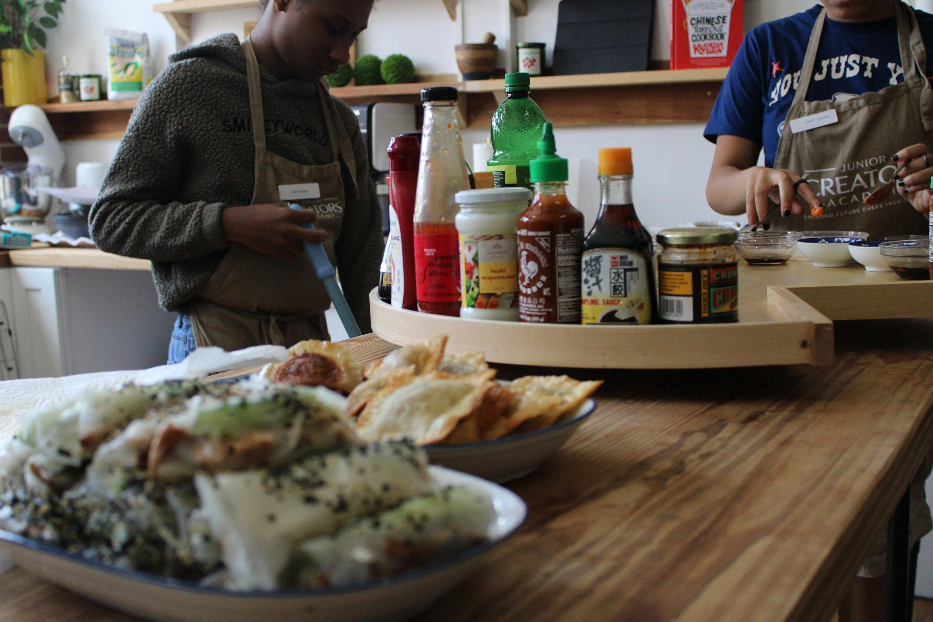 People wearing aprons preparing food in a kitchen with ingredients on the table