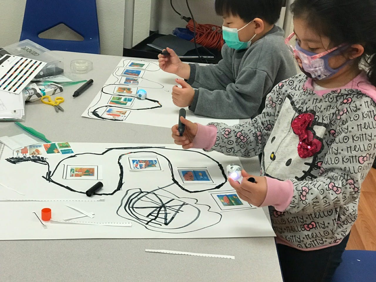 Two children in masks drawing on large sheets of paper