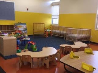 Empty classroom with small tables and chairs, cribs, and toys