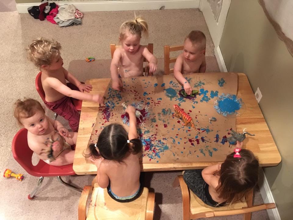 Multiple children sitting around a table covered in paint