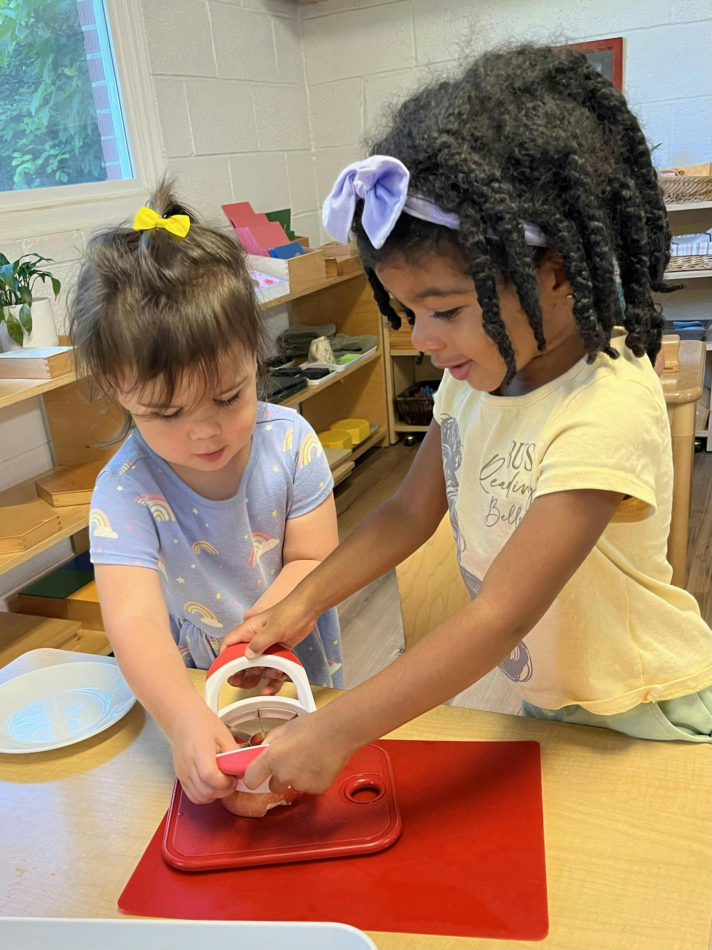 Two children using a food chopper on a red cutting board