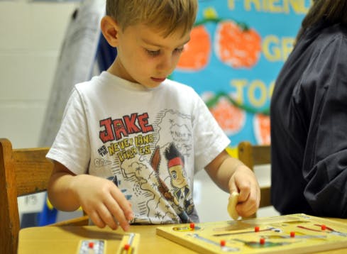 Child playing with a wooden maze puzzle on a table