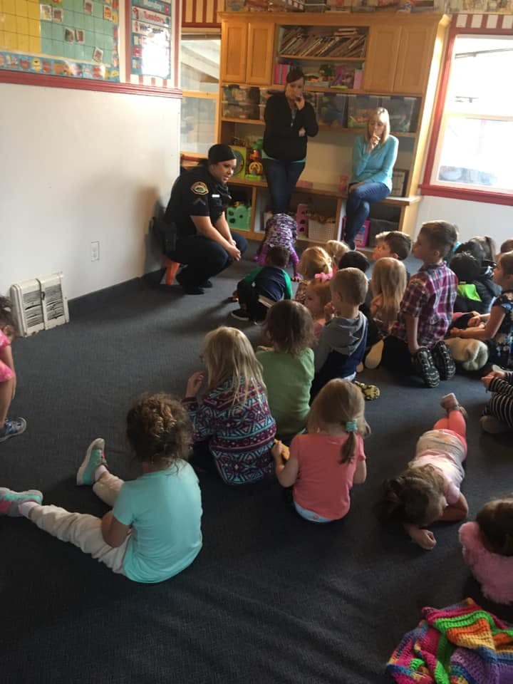 Person in uniform kneeling and speaking to a group of children