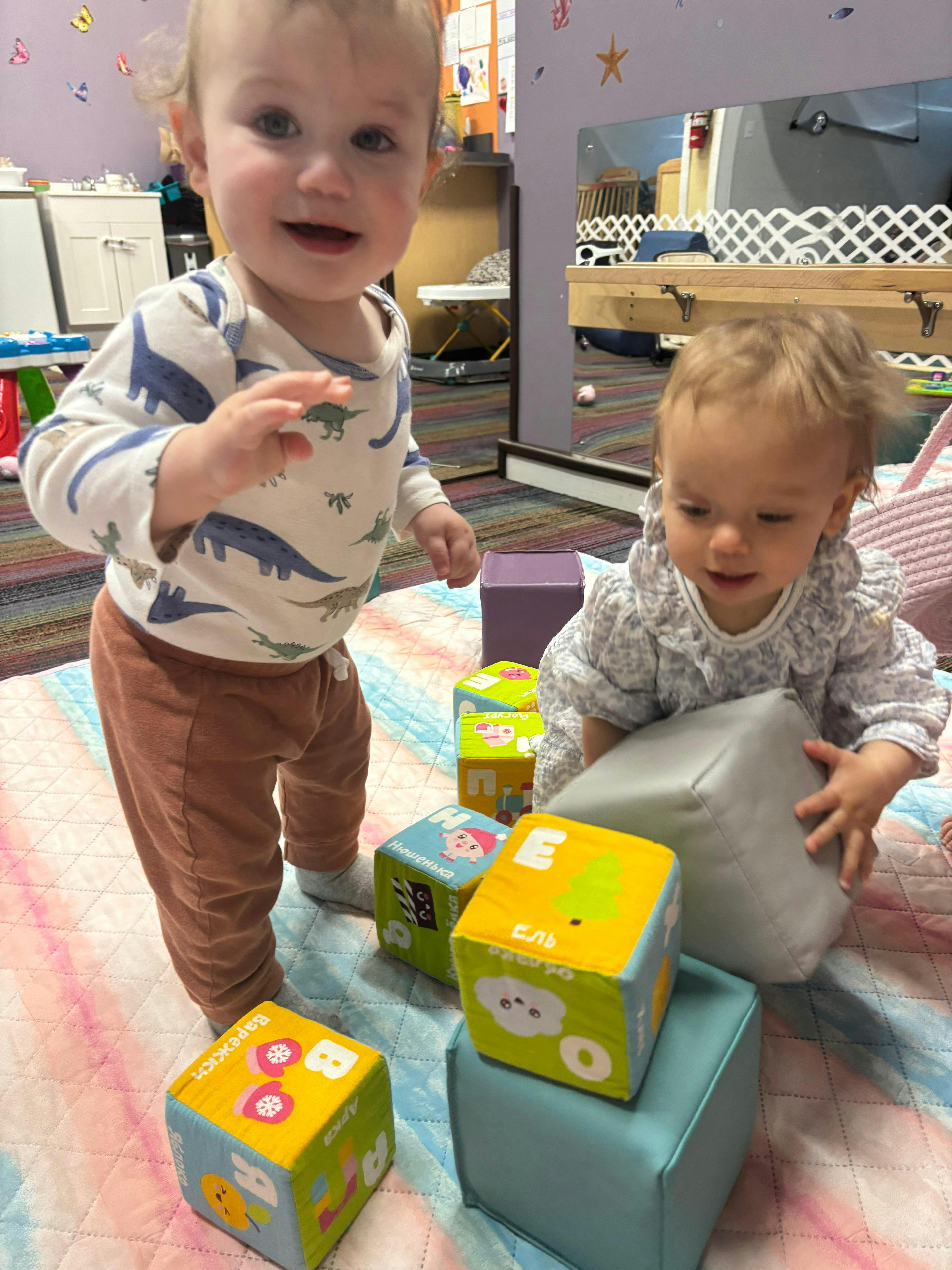Two children playing with soft toy blocks on a floor mat