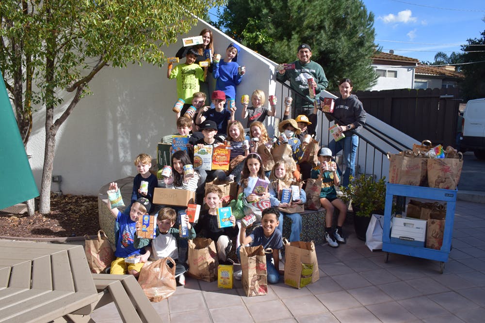 Group of adults and children posing with bags of donated food items