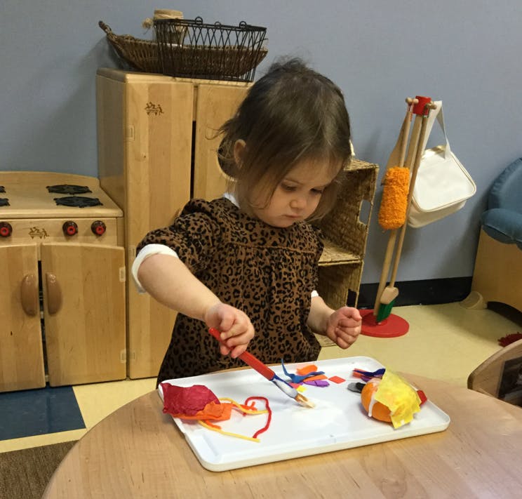 Child painting with yarn and other craft materials on a tray