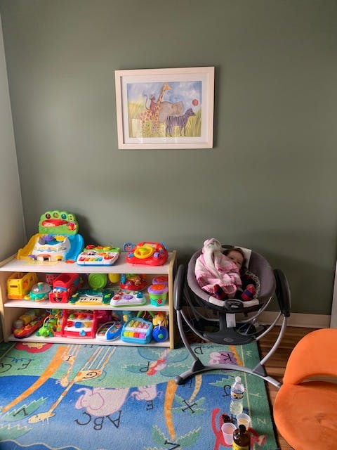 Child sleeping in a baby swing next to a shelf of toys