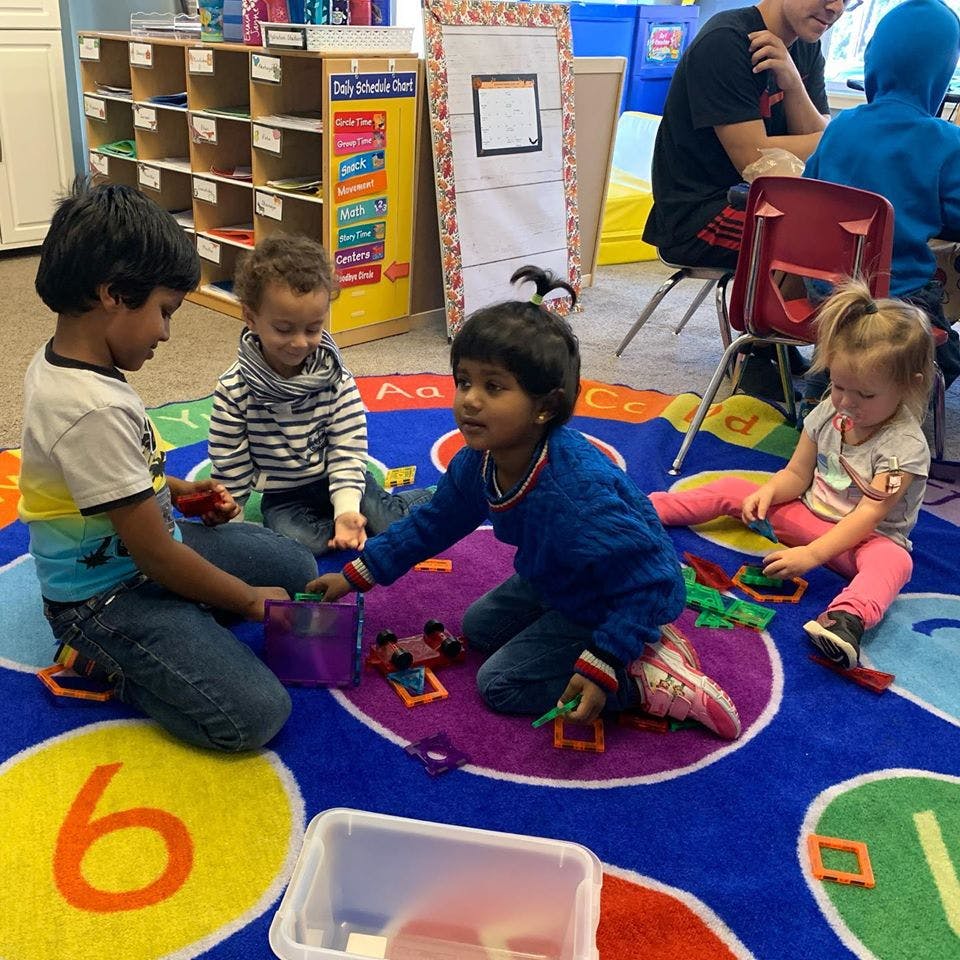 Four children playing with toys on a colorful rug in a classroom