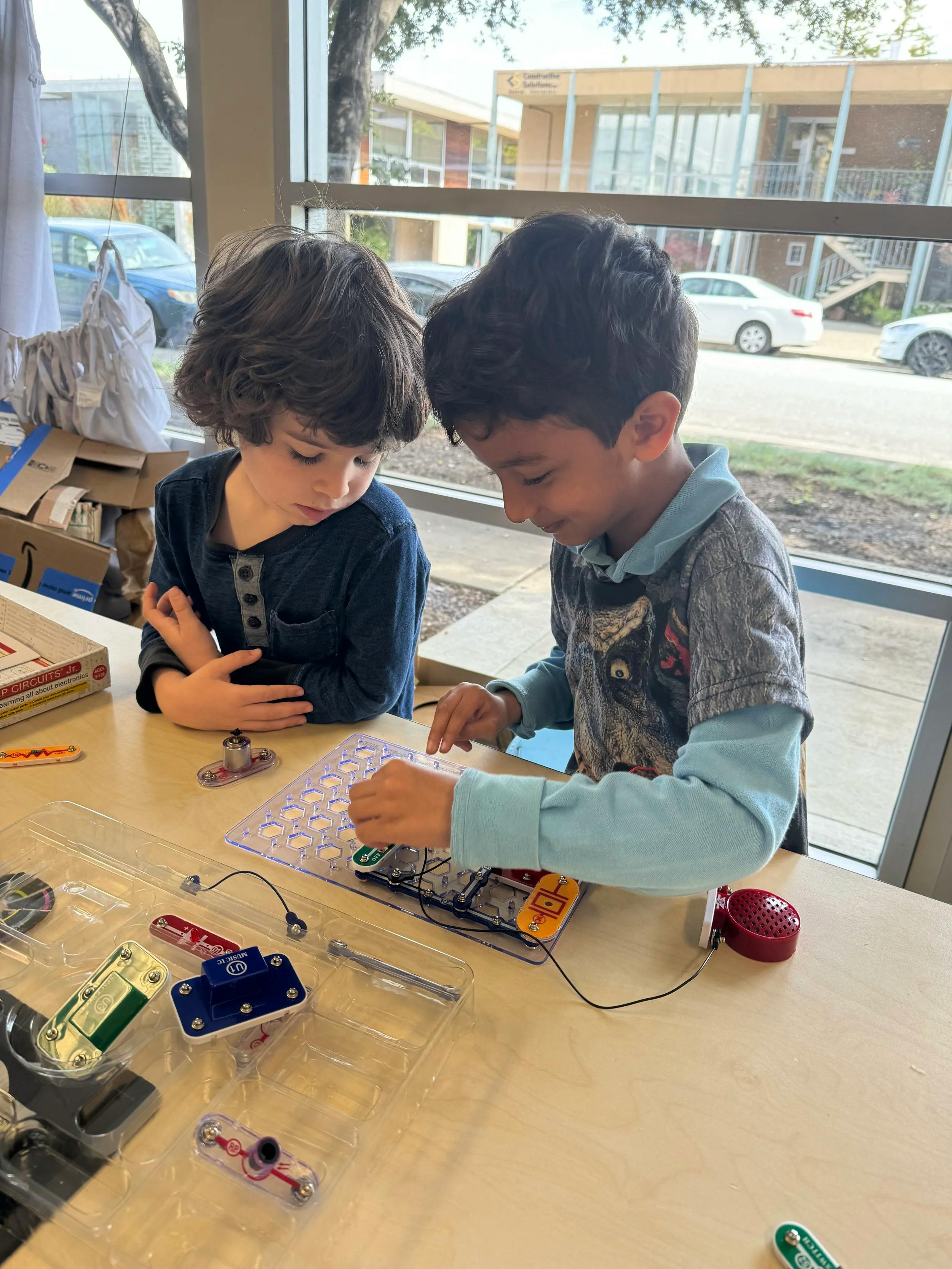 Two children playing with an electronics kit at a table