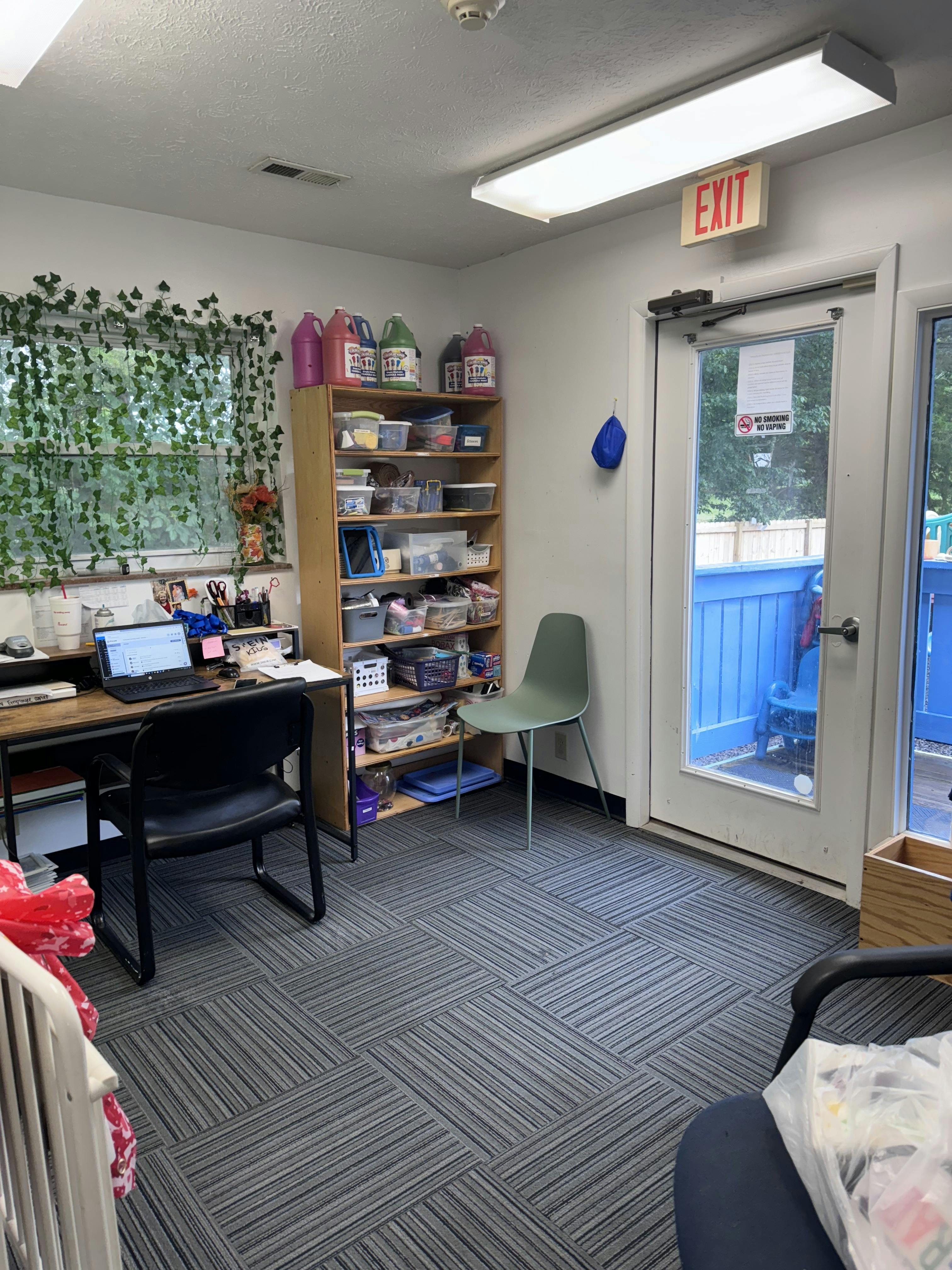 Office room with a desk, shelves with supplies, and an exit door with a no smoking sign