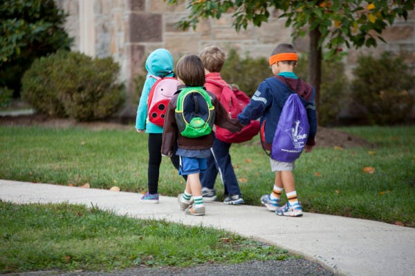 Four children with backpacks walking on a sidewalk