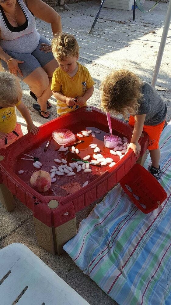 Two children playing with ice and water in a red sensory table