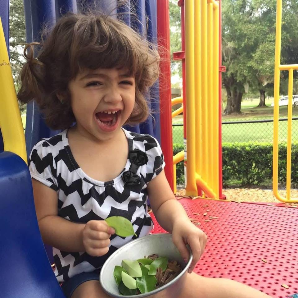 Child holding a bowl with leaves and a single leaf in hand on a playground