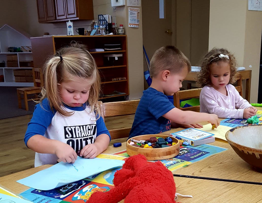 Three children sitting at a table doing an activity