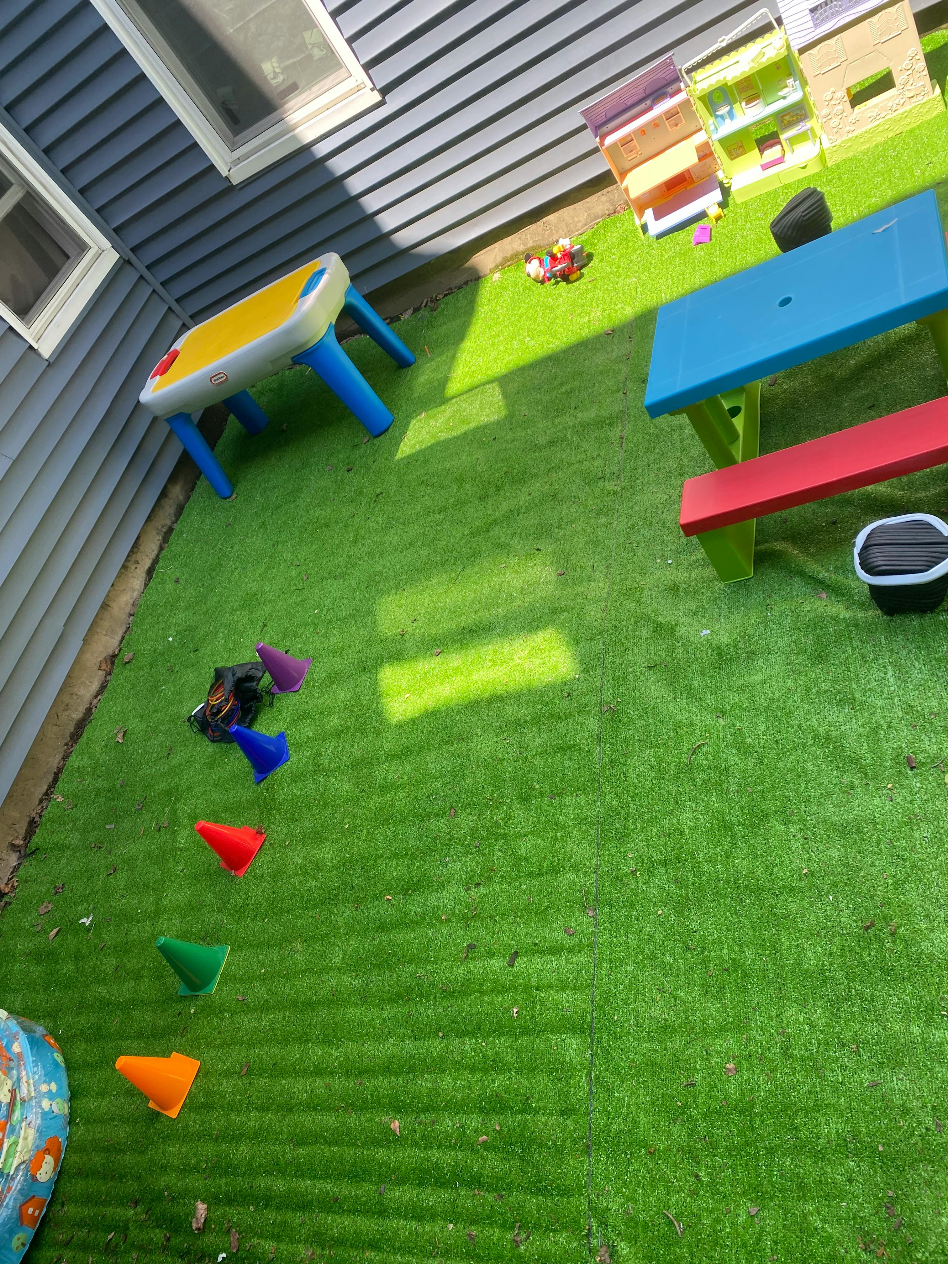 Overhead view of a play area with playhouses, a table, and cones on artificial grass
