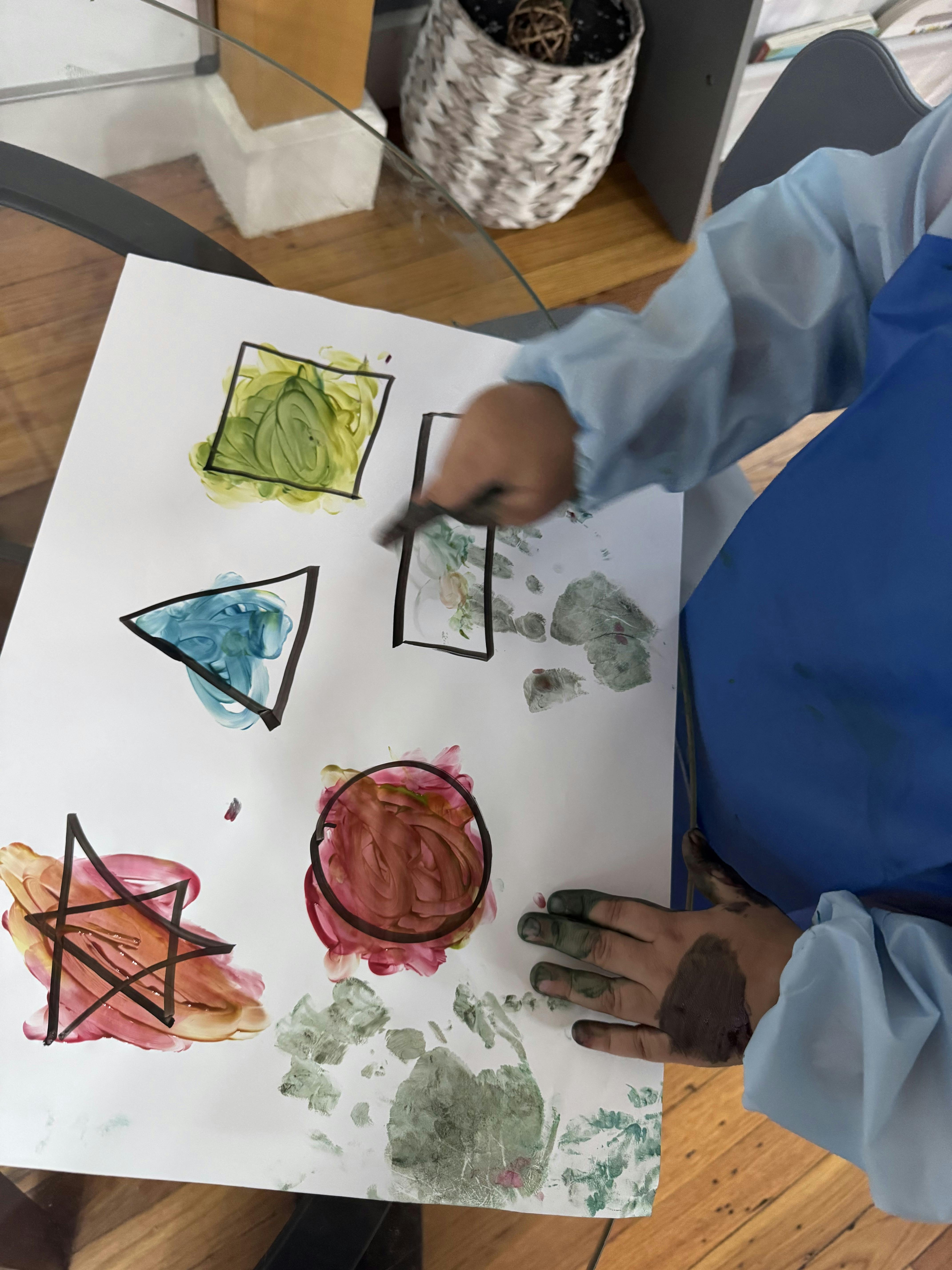 Child painting inside outlined shapes on paper