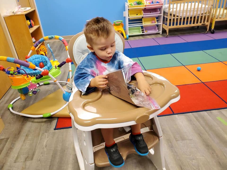 Child in a high chair holding a brown paper bag