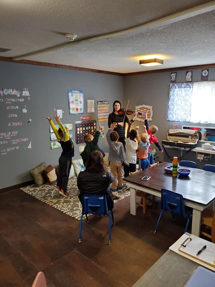 Adult playing violin for children in a classroom