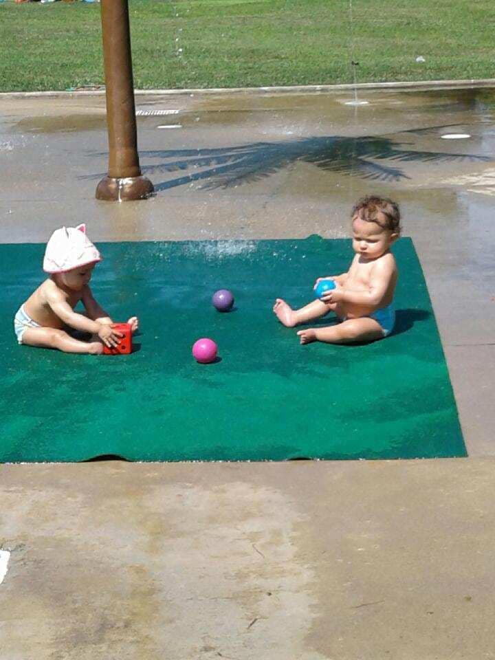 Two children playing with toys on a green mat in a splash pad
