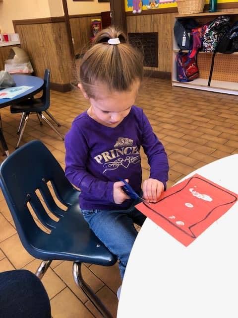Child cutting red paper with scissors at a table
