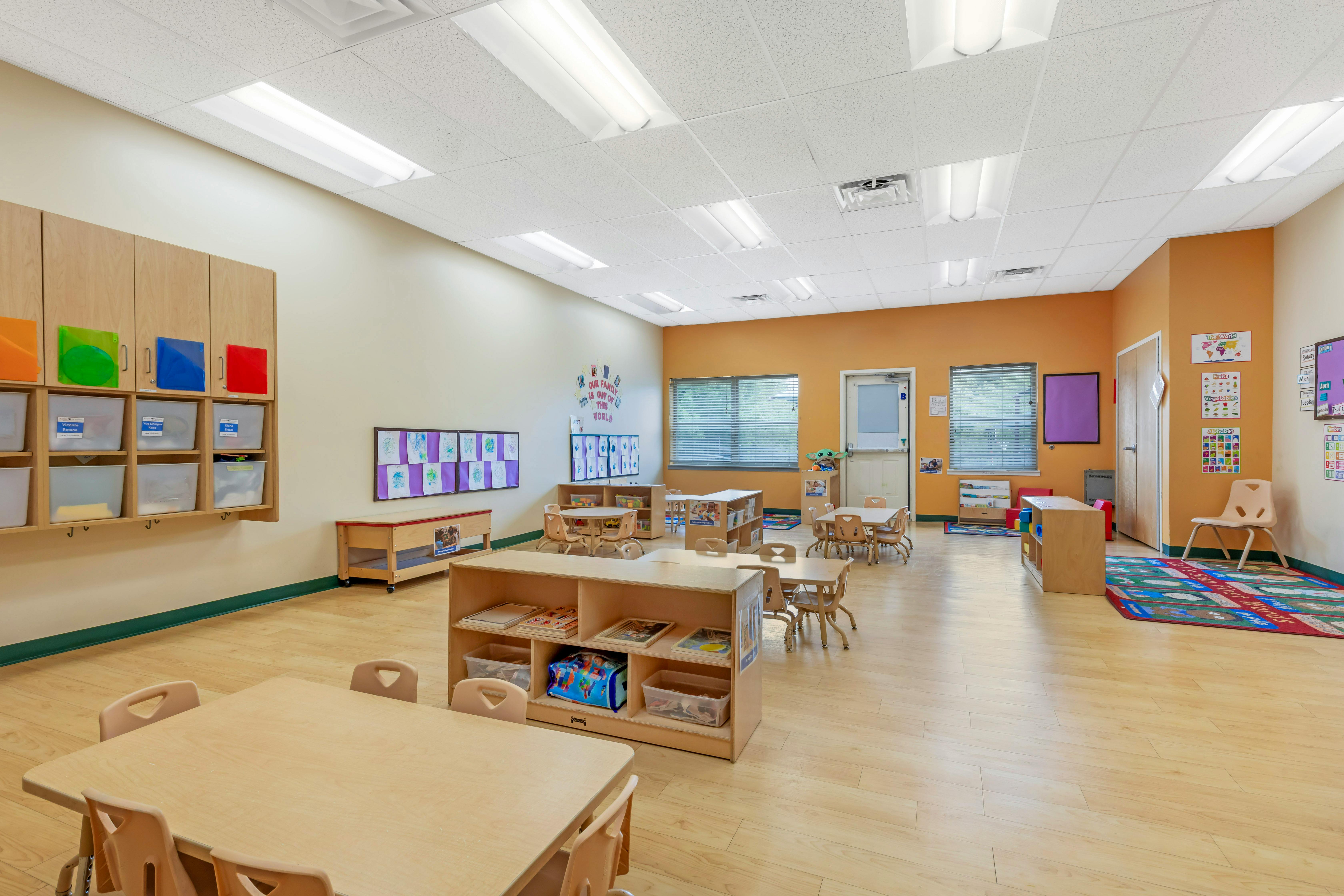 Empty preschool classroom with small tables and chairs and storage shelves