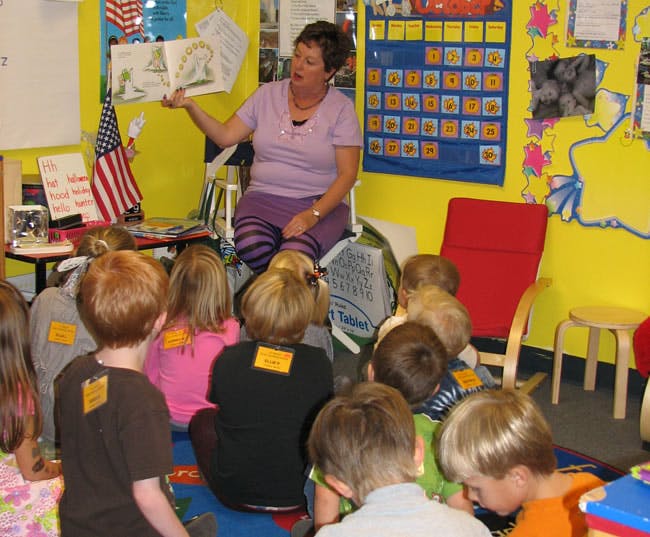 Person reading a book to a group of children in a classroom