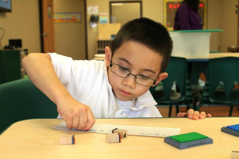 Child with glasses stamping on paper at a table