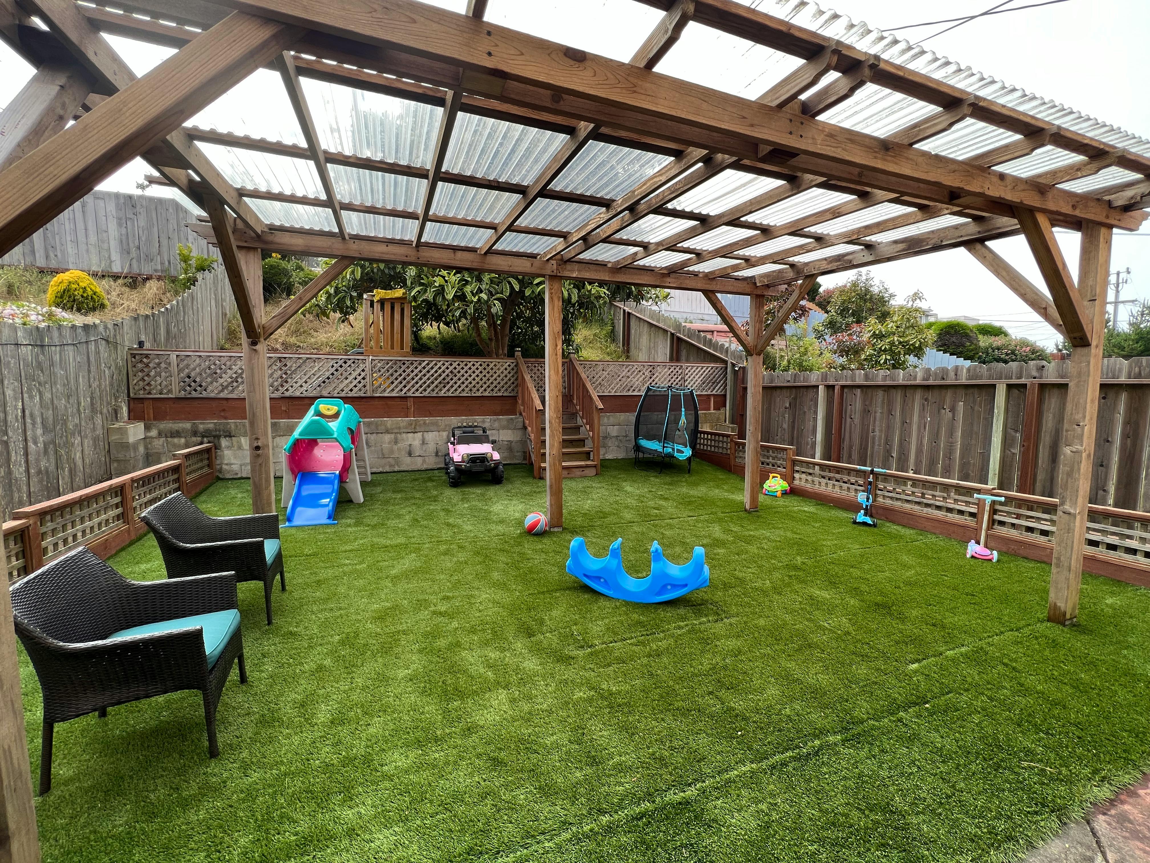 Backyard with artificial turf, a wooden pergola, and children's play equipment