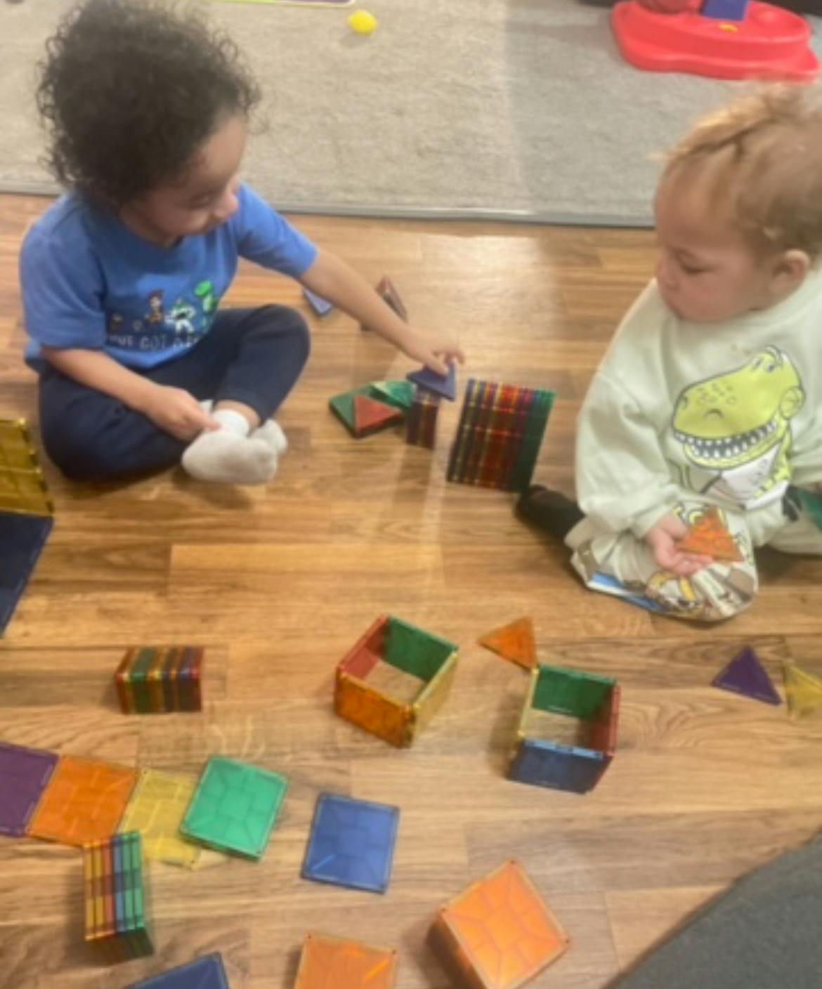 Two children playing with colorful magnetic tiles on a wooden floor